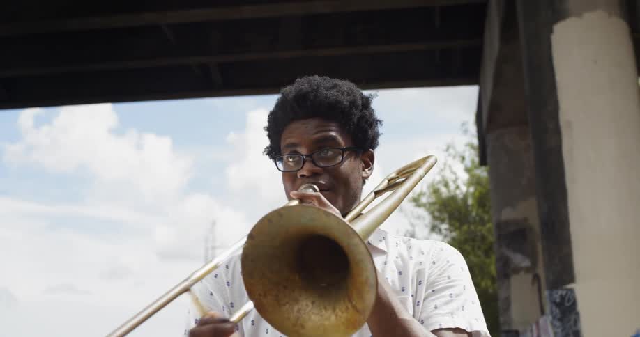 Young black man plays trombone outside under bridge