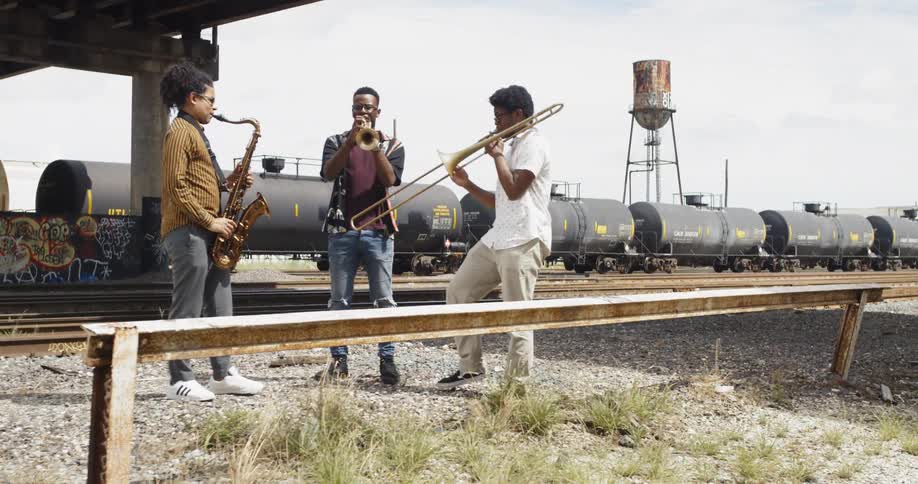 Three musicians play near stopped train on train tracks
