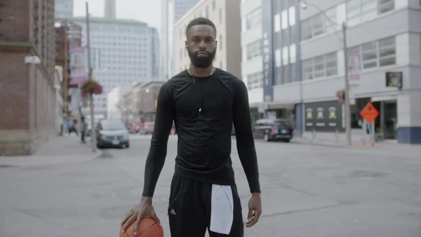 A black man stands on a city sidewalk while holding a basketball