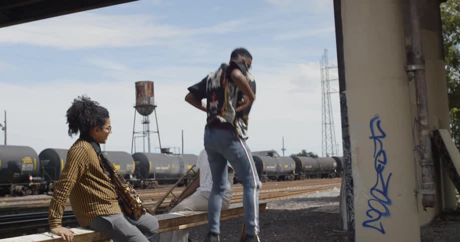 Three men are sitting near a railroad track playing music