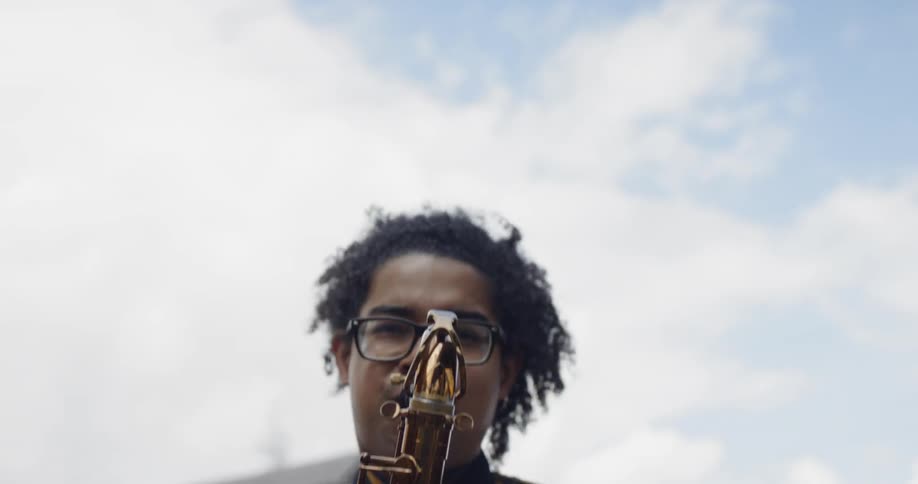 Long haired black man plays saxophone outdoors