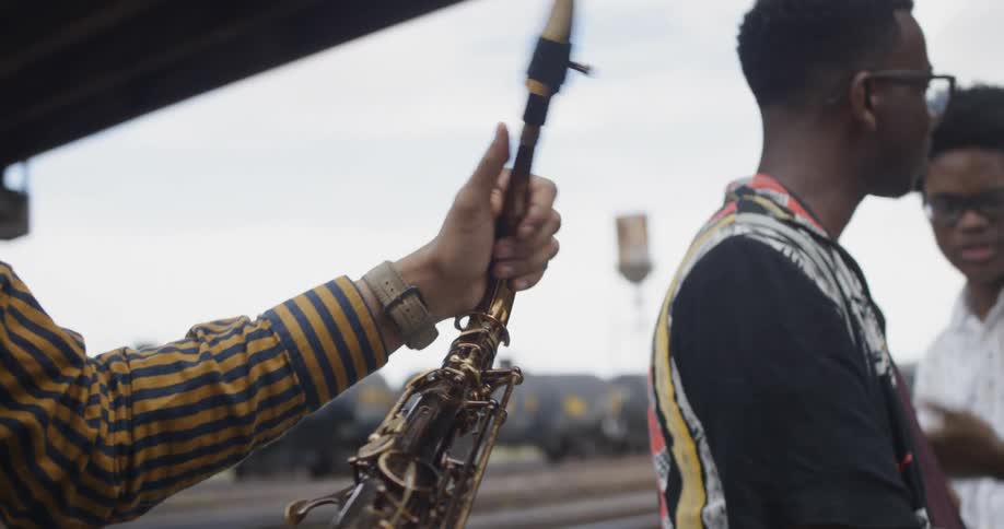 Three young black men with musically instruments talking by a train track