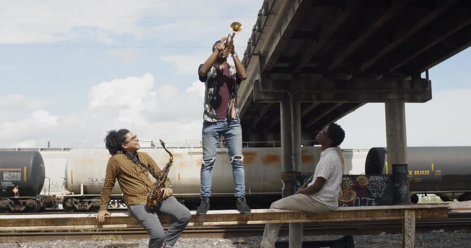 Three young musicians playing instruments near the train tracks