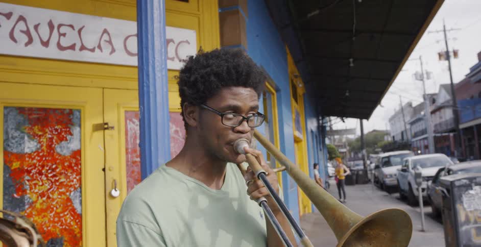 Three black man play saxophone outdoors in front of a yellow door in the street
