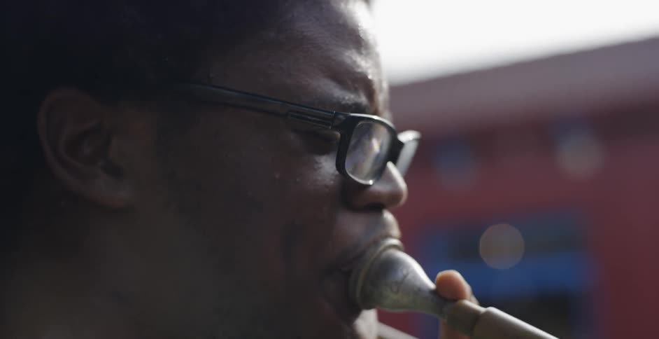 A close of up of a African man playing the horn maybe a saxophone it looks like he is walking maybe in a parade