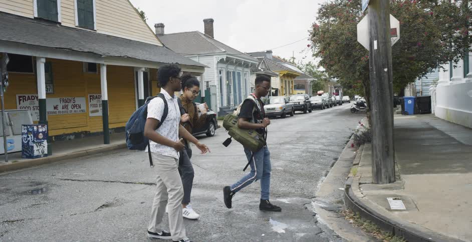 Three young black men walk across a street in a neighborhood