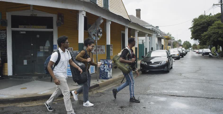 Three men with bags on their shoulders walk across a road
