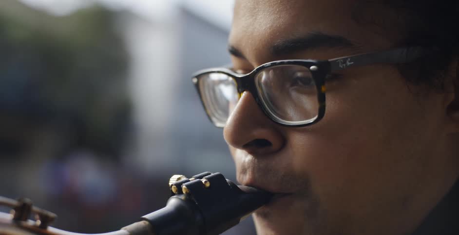 Young black man in glasses plays saxophone outdoors