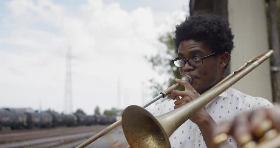 Two black men play musical instruments near railroad tracks