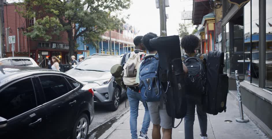 Three teenagers walking down the street with backpacks and instrument cases