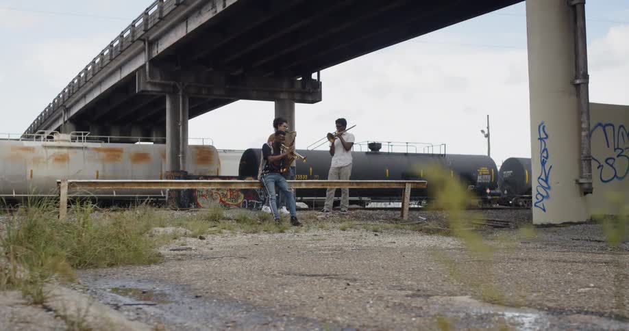 Three people playing instruments next to a train
