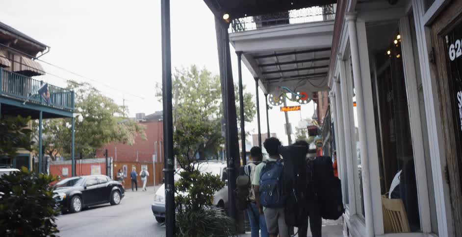 Three young black men with backpacks walk down a sidewalk in the city