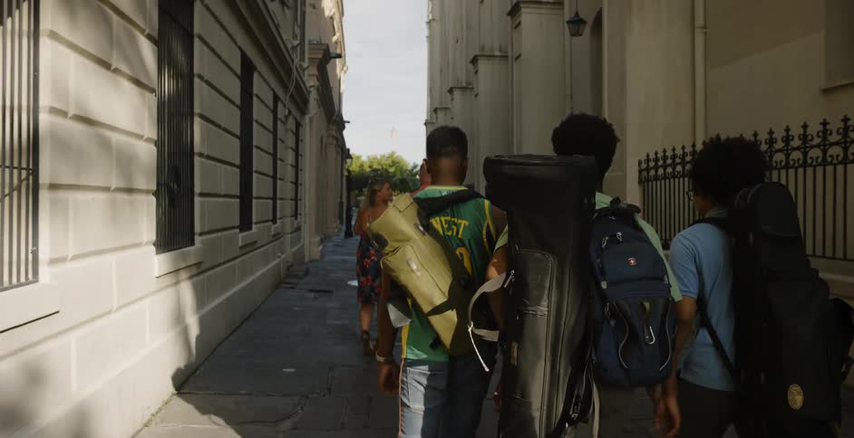 Three young black men carrying instruments walk down an alley in a city