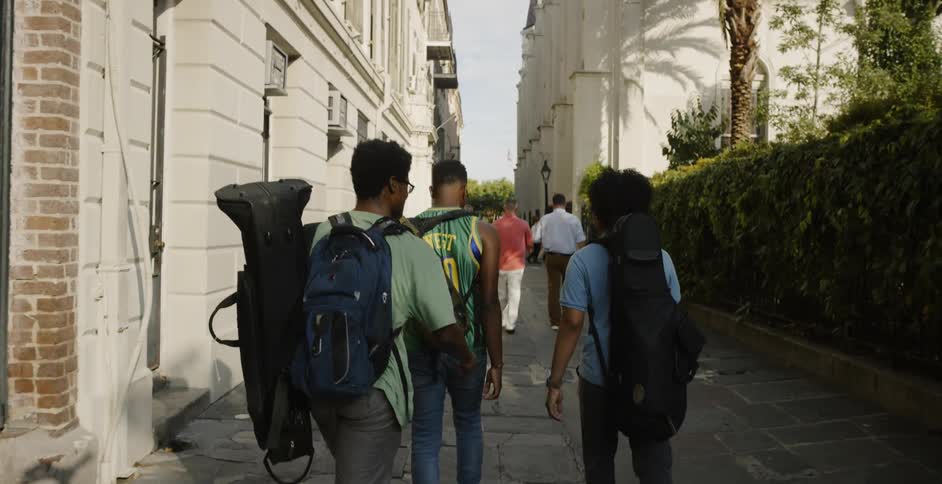 Males walking on a path carrying backpacks and instruments in the city
