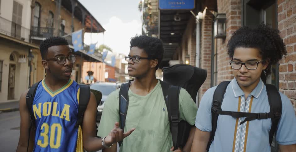 Three men walk along sidewalk wearing backpacks
