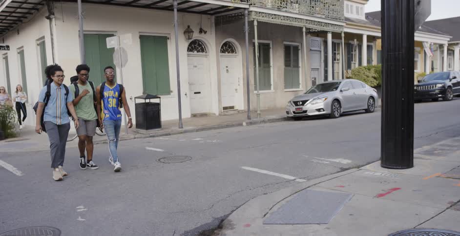 Three young black men walk on a crosswalk passing other pedestrians
