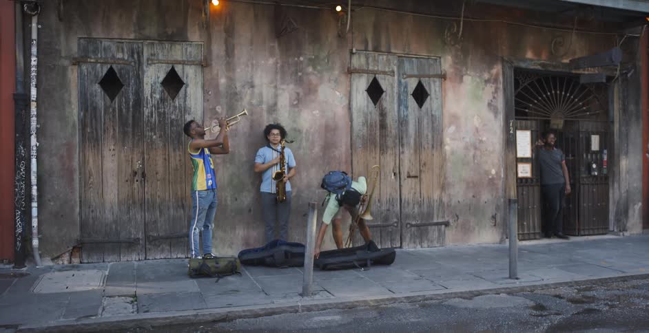 Group of three black men playing their musical instruments in front of an old building