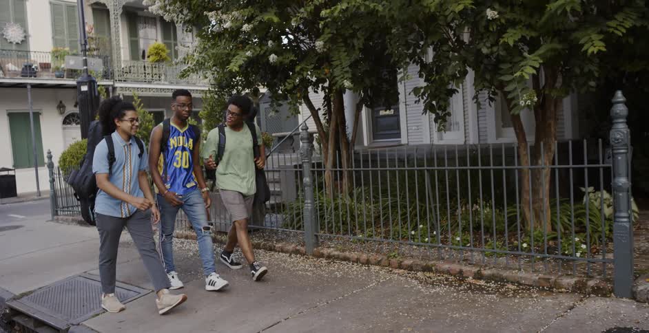 Three young black men talk as they walk down a neighborhood sidewalk