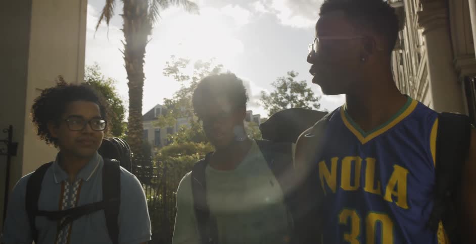 Three black boys wearing glasses and backpack walk down in the street on a sunny day