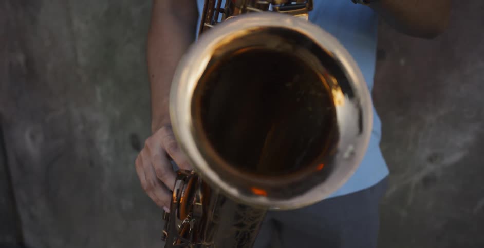 Man wearing wristwatch plays saxophone in front of wall outdoors