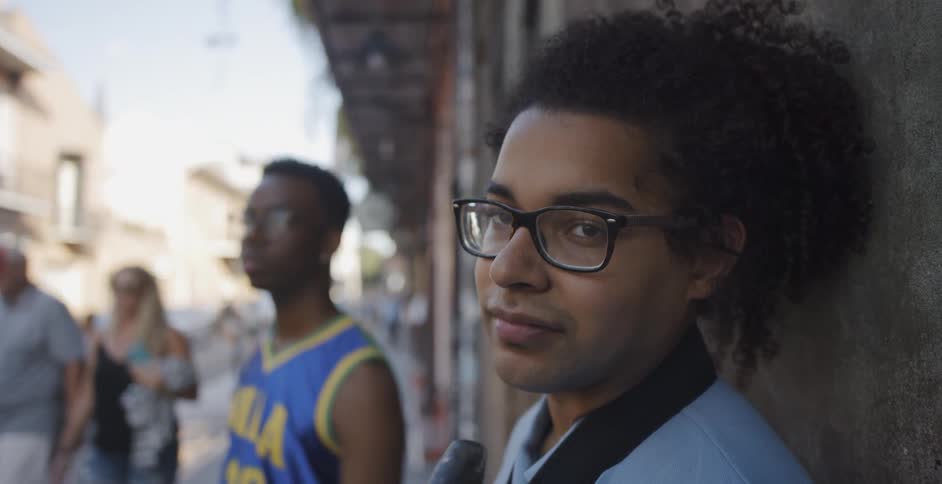 Young black man stand at the wall and looks to the camera while people go around him