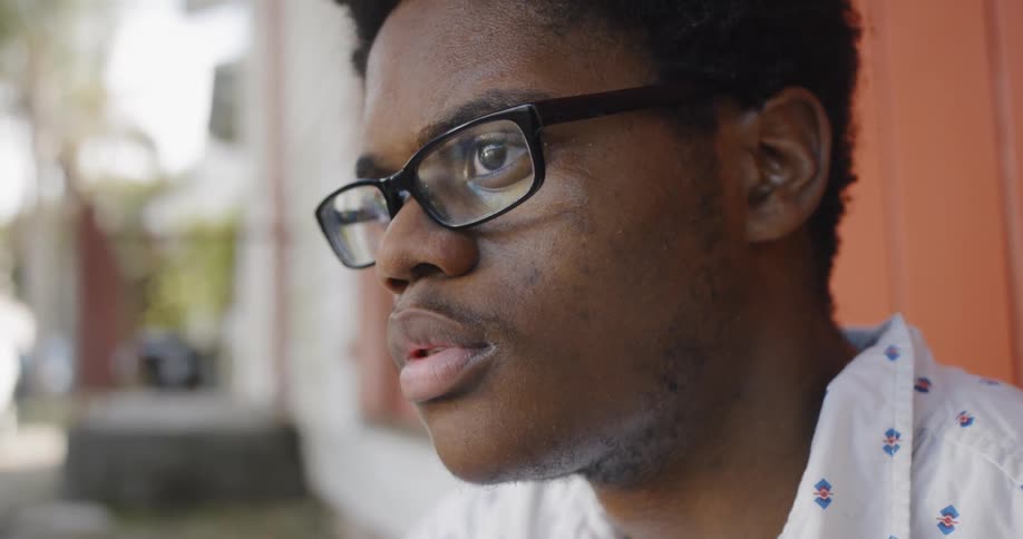A black man in deep thought sits outside a building