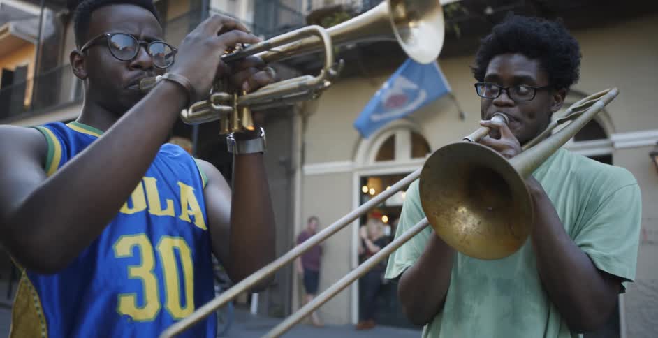 Two black men play a trombone and a trumpet in a city street