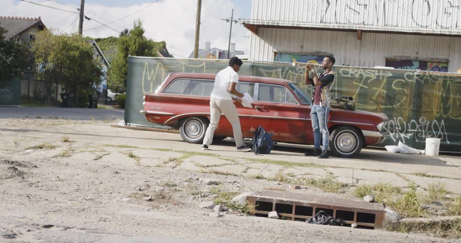 Black men rehearsing with their musical instruments in front of a red car