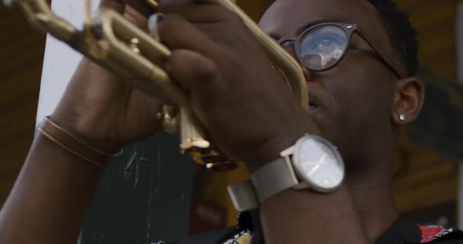 Man plays a trumpet while standing next to a pillar