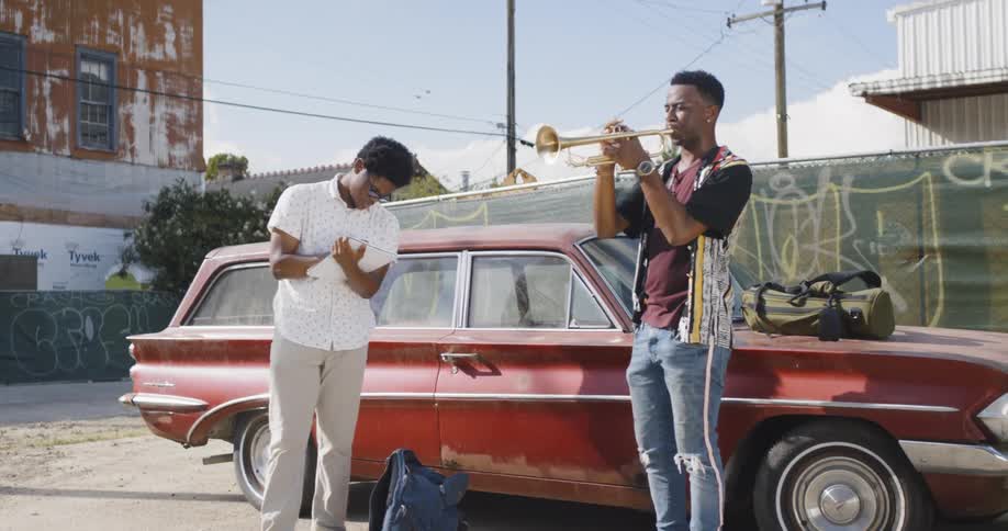 Two people play music next to a car