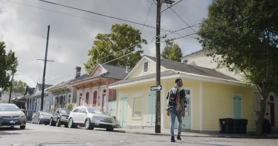 A man with a trumpet in his right hand walks across a residential street