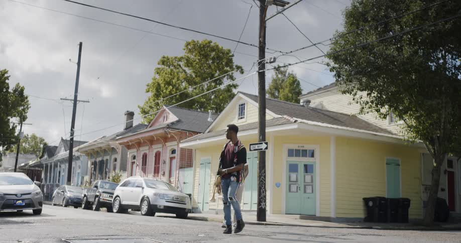 Two young black men walk across a neighborhood intersection while talking and smiling