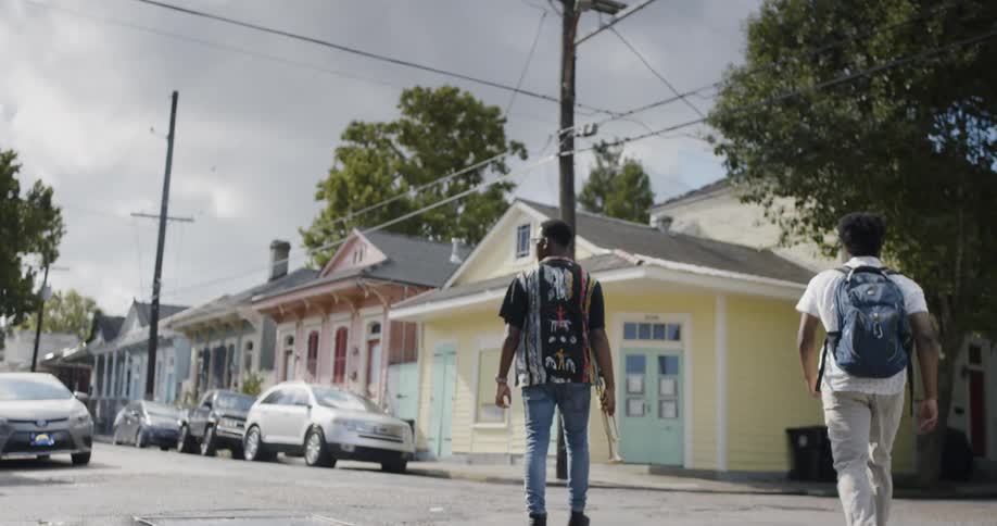Two black boys carrying saxophone and backpack cross the road on a cloudy day in the daytime