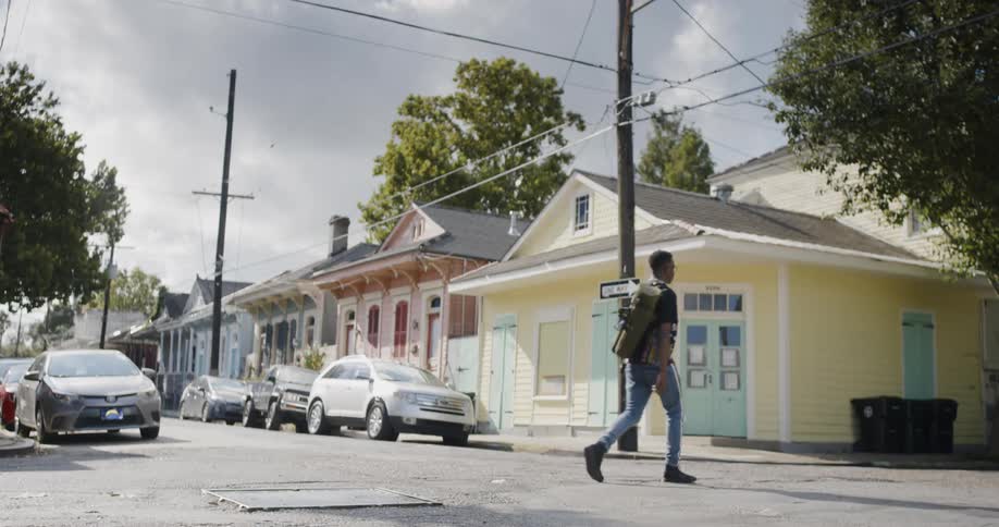 A young black man with a duffel bag walks across a neighborhood street