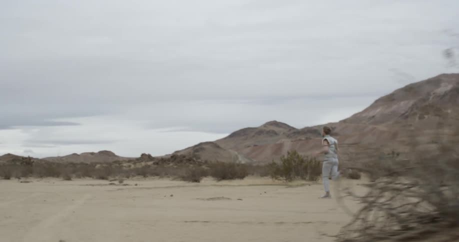 Man runs in the desert very fast and you see mountains in the background