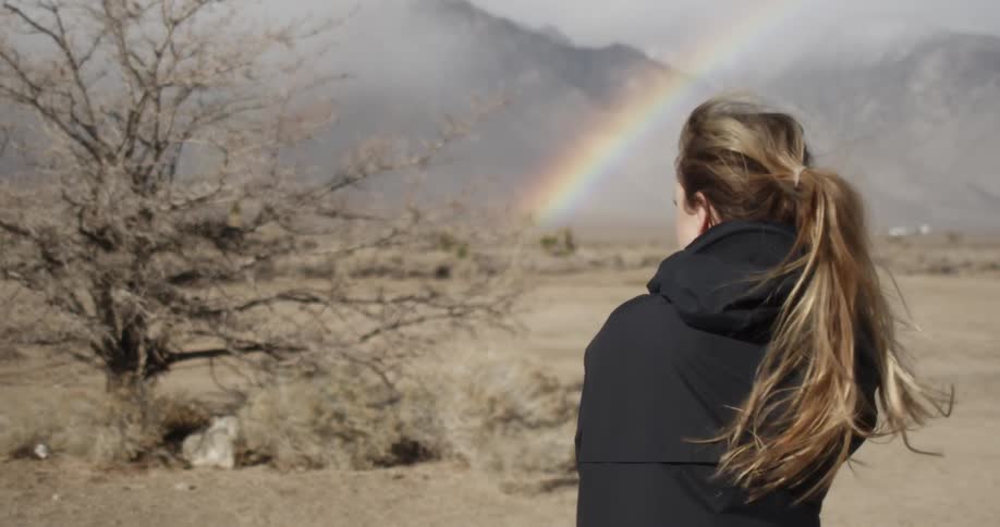 A woman stares off into the distance at a rainbow
