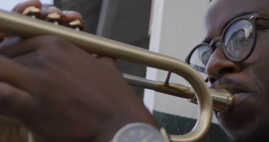 A black man with glasses plays a trumpet