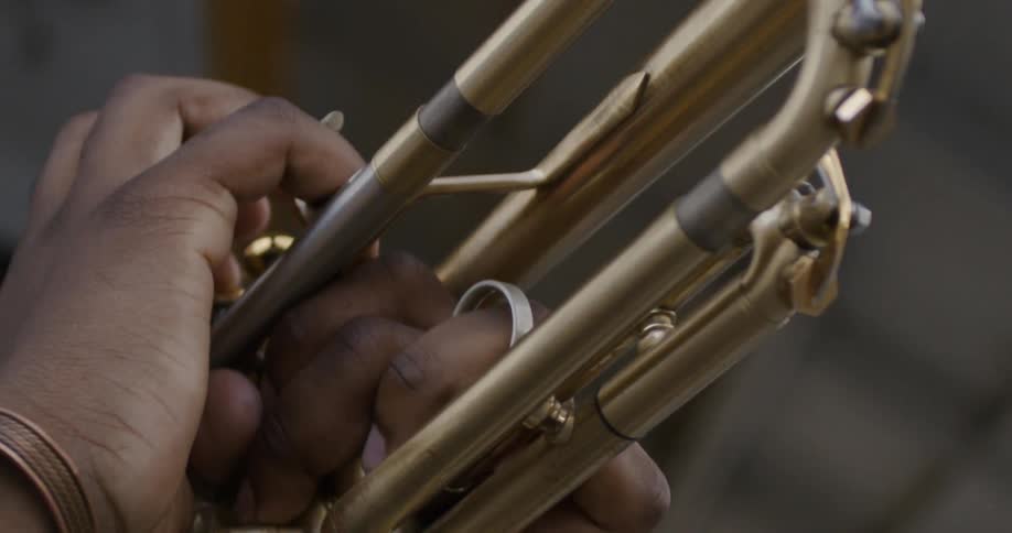 A black person's hands are seen holding the body of a brass trumpet as they play it