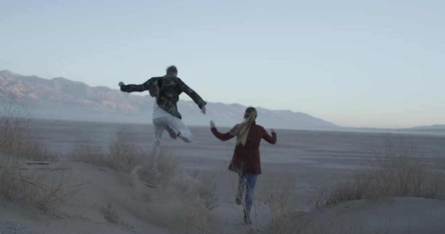 Man and woman run happily on vast open sand field at dusk