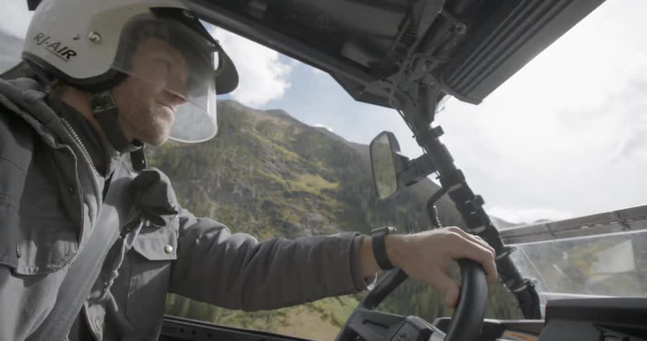 Man wearing helmet drive vehicle in rough terrain near mountain