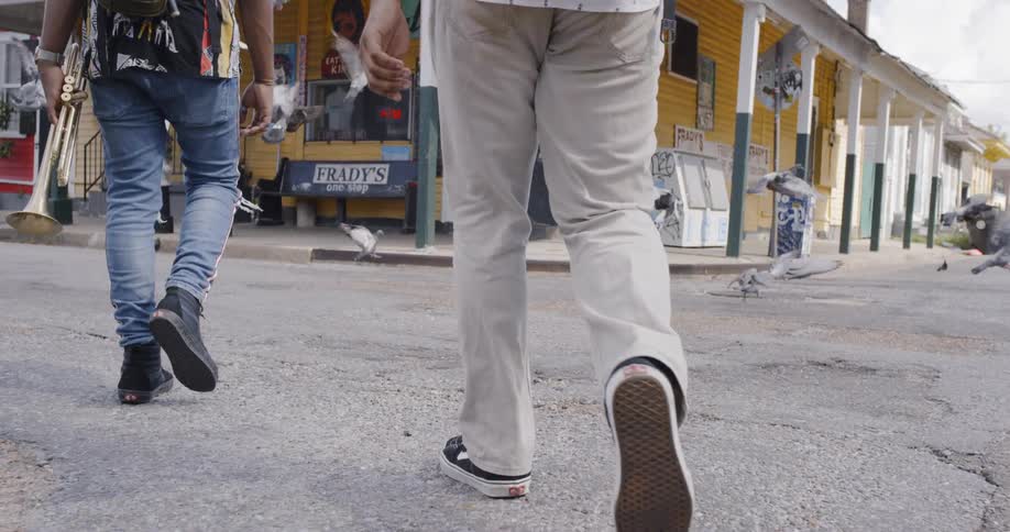 Two people walking down the street holding an instrument surrounded by pigeons