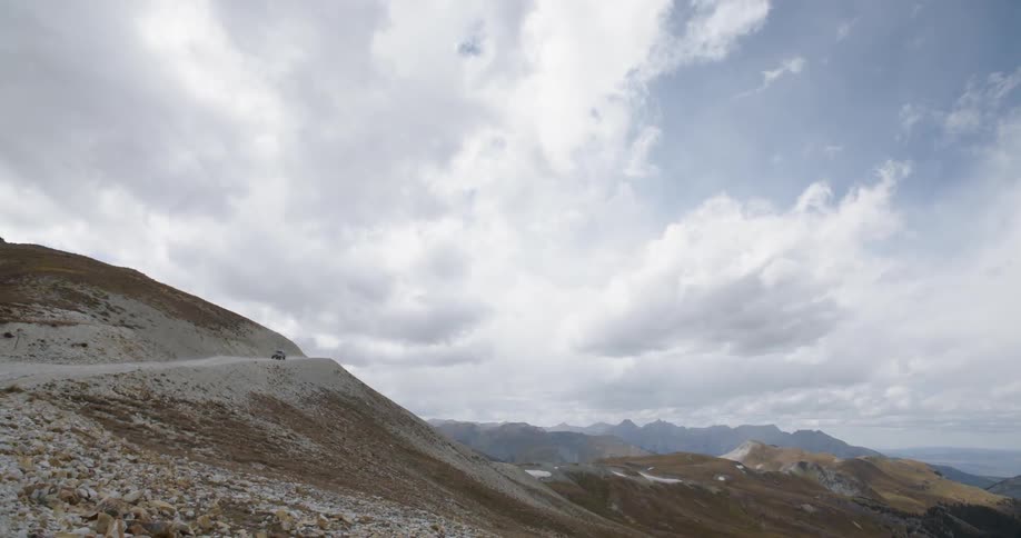 Camera looks towards the sky and mountain range as a vehicle comes down a trail
