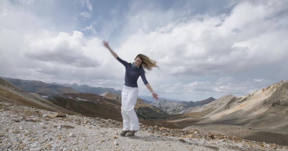 A woman smiles and jumps as she stands in front of a mountain range