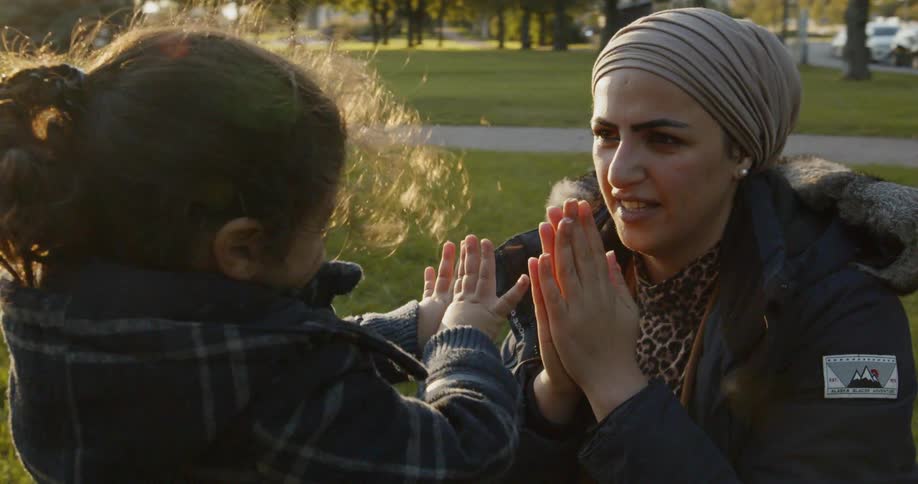 A woman and child playing patty cake in a park