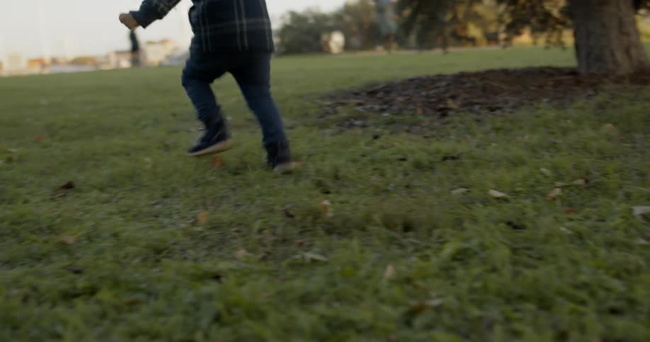 A child runs across a lawn in a park at low sun