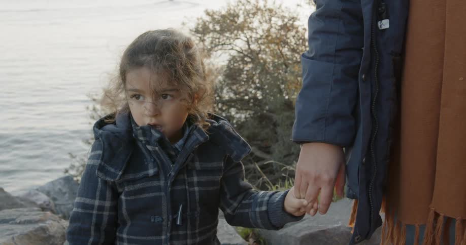 A young girl holds her parents hand next to the water