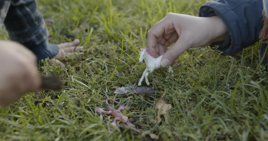 Two people play with animal figurines in grass