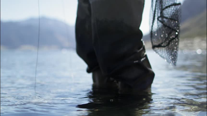 A fisherman is fly fishing in shallow water