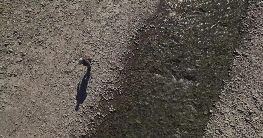 A fisherman walks along a stream carrying his fishing pole