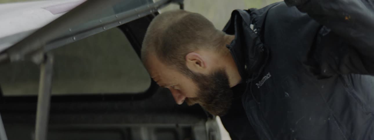 A white man opens the back of his vehicle and checks a tool